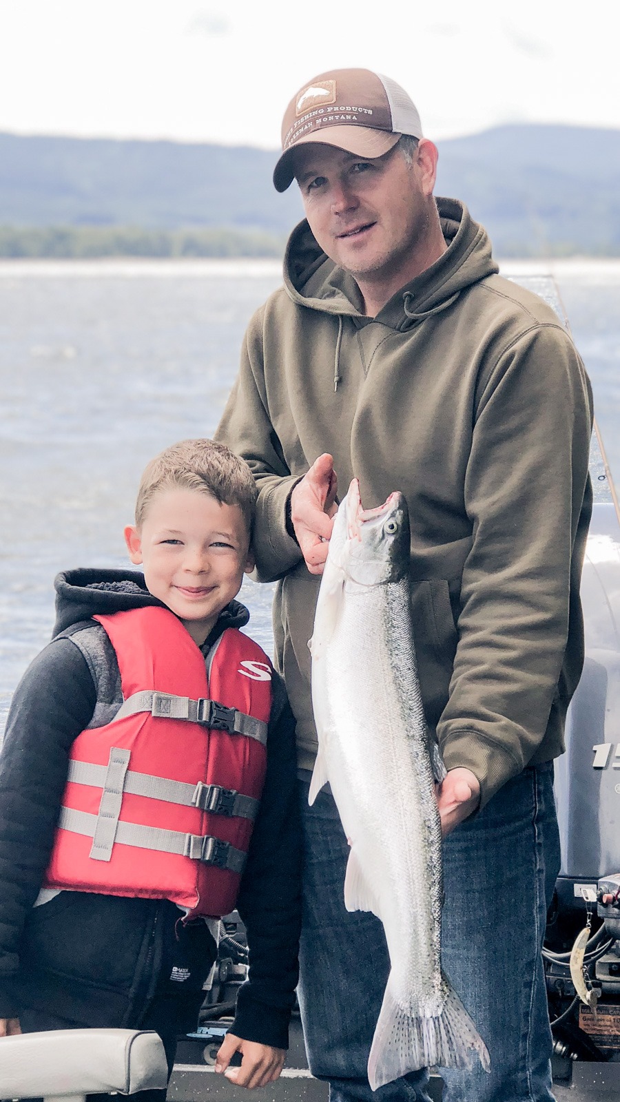 Fishing guide, Mike Hazen, holds summer steelhead on the Columbia River with his son