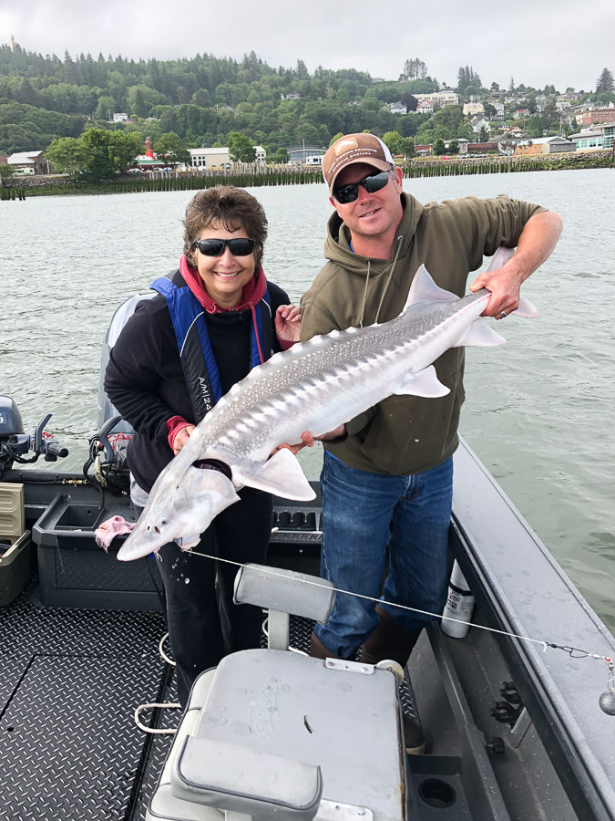 Woman poses with sturgeon she caught on the Columbia River near Astoria with fishing guide Mike Hazen
