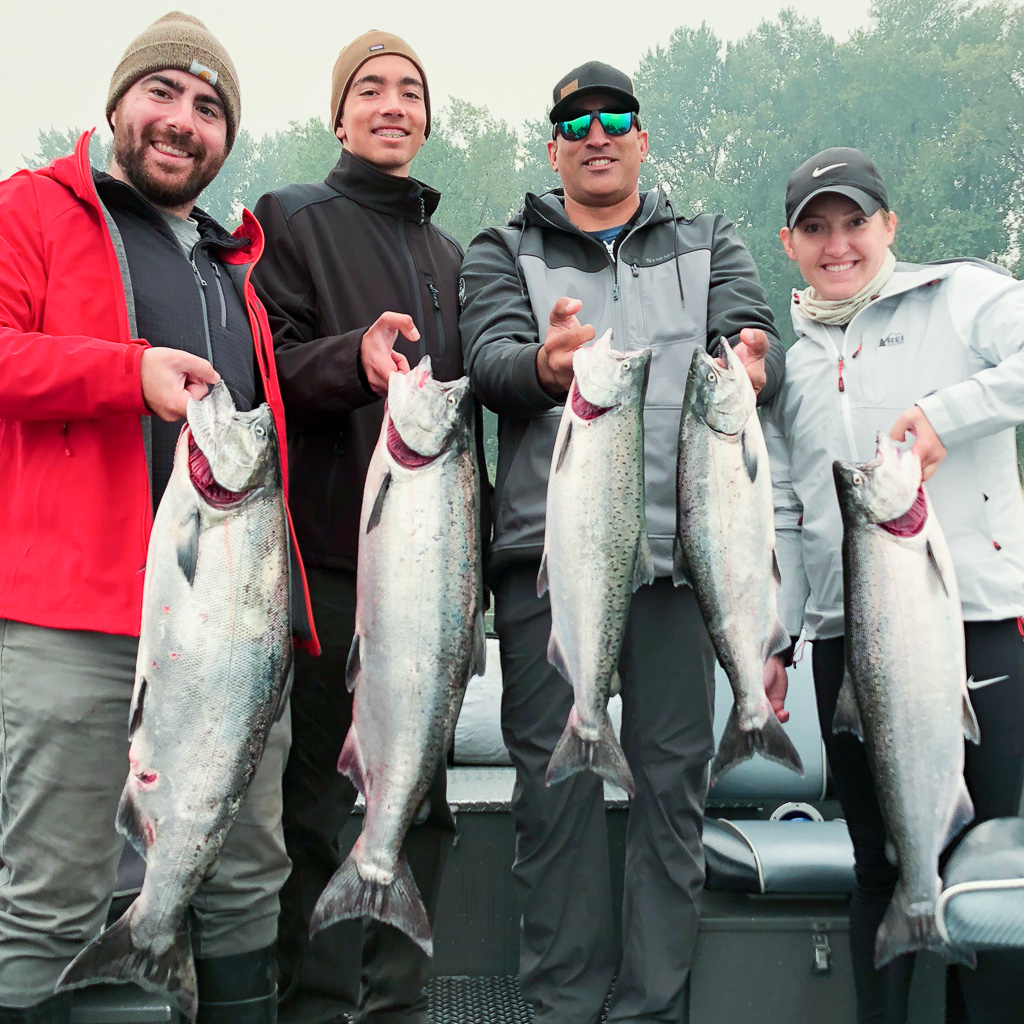 Four people hold up the Fall Chinook Salmon caught fishing on the Columbia River with a fishing guide