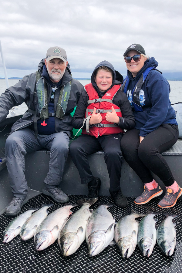 Man, woman, and young boy pose for a photo in a boat with 8 fish they caught at buoy 10