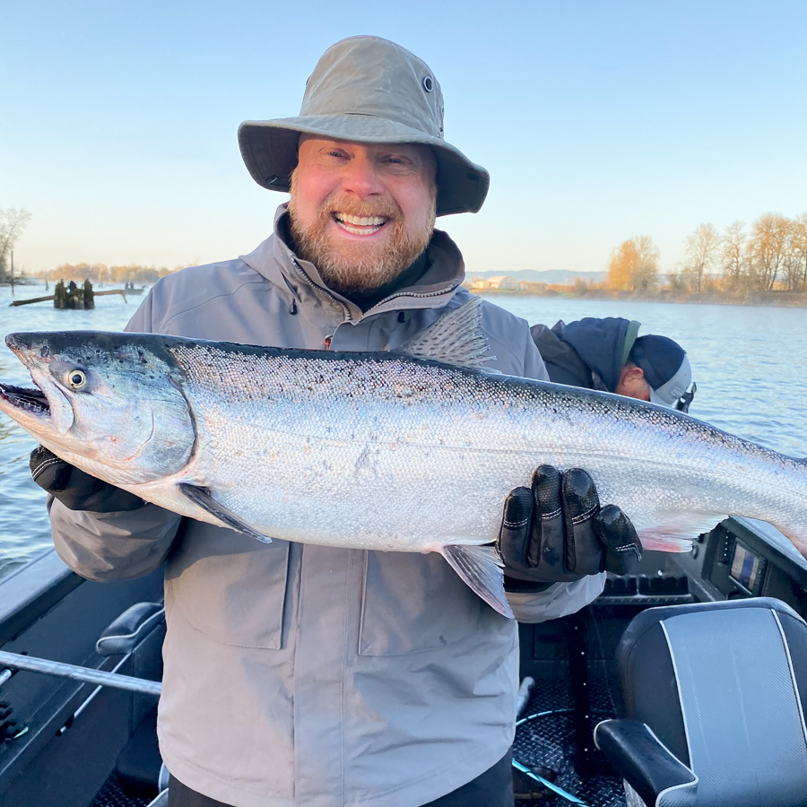 Man proudly smiles as he holds up a spring chinook salmon he caught on the Multnomah channel of the Willamette river