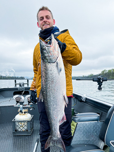 Man holds up a large Spring Chinook Salmon on a fishing trip on the Columbia River he booked with a fishing guide